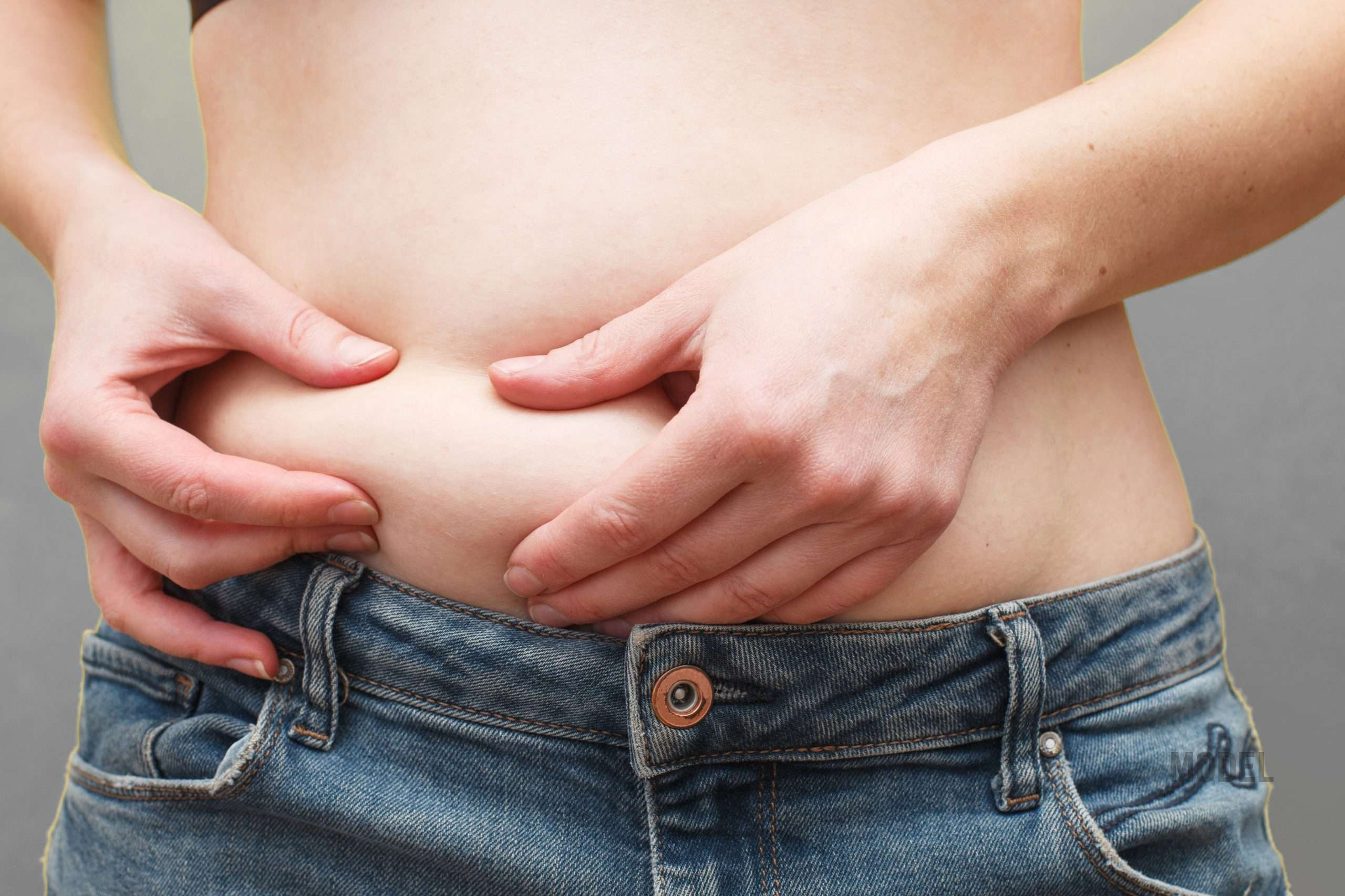 Woman pinching loose abdominal skin representing muffin top after tummy tuck, liposuction contour concerns, and non-surgical body contouring options